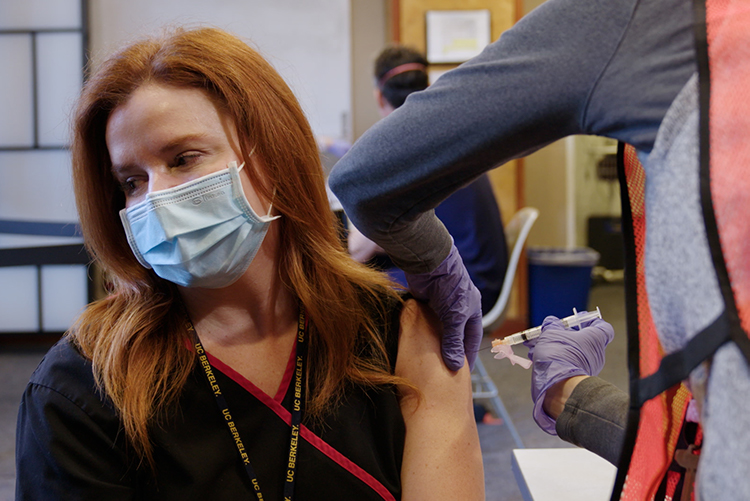 A nurse with red hair gets the COVID-19 vaccine while wearing a mask