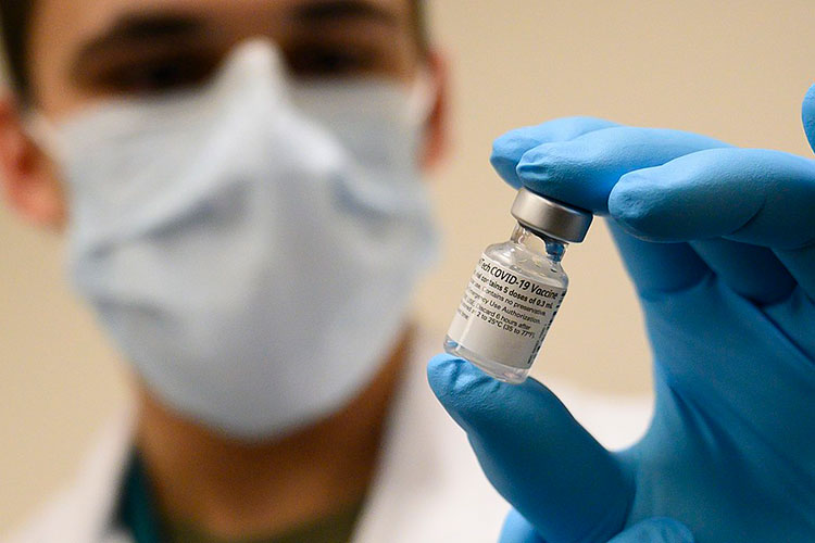 A photo of a gloved hand holding a vial of COVID-19 vaccine