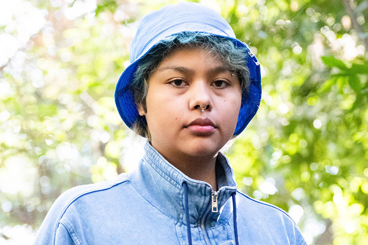 A close-up photo of Cheyenne Two Feathers Tex, a senior at UC Berkeley and a Native American who supported the unnaming of Kroeber Hall. She is standing by Strawberry Creek.