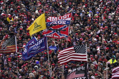 A crowd of Trump supporters carrying various flags, including the confederate flag emblazoned with a rifle