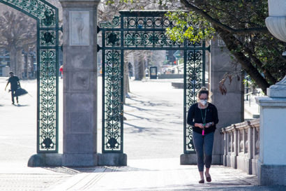 A woman in a face masks walks near Sather Gate.