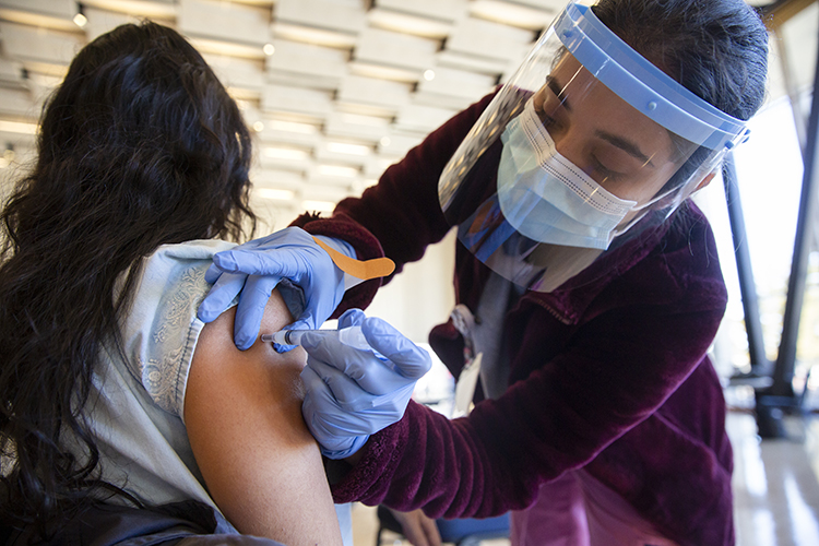 Cecilia Mejia receives a COVID-19 vaccine in Pauley Ballroom from Andrea Gomez, a University Health Services nurse. The fourth-year conservation resources studies student is a senior residence hall assistant, in Blackwell Hall.