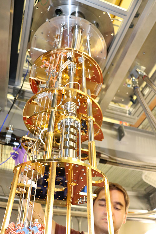 A photo shows a large gold colored cylinder, with a student adjusting things nearly the bottom.