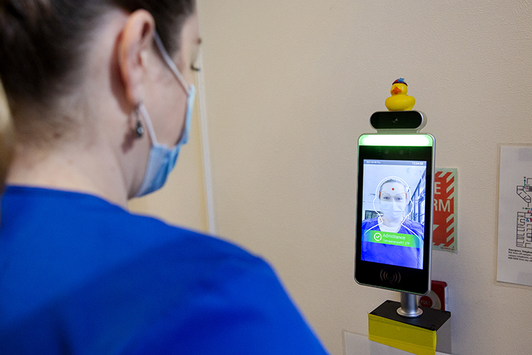 In Minor Hall, an employee demonstrates the new contactless facial recognition temperature scanner that is part of patient check-in. The screen is the size of a large cell phone and on a stand.