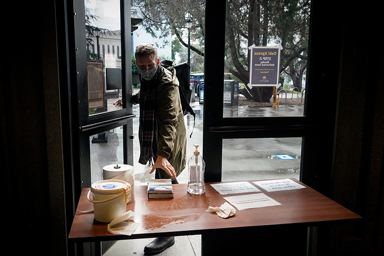 A book borrower reaches through a doorway to Moffitt Library to grab a book off a table as part of the contactless Oski Xpress book borrowing service.