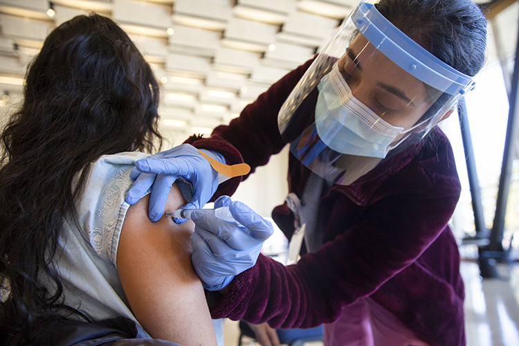 a woman in a face mask gives a vaccine to another person