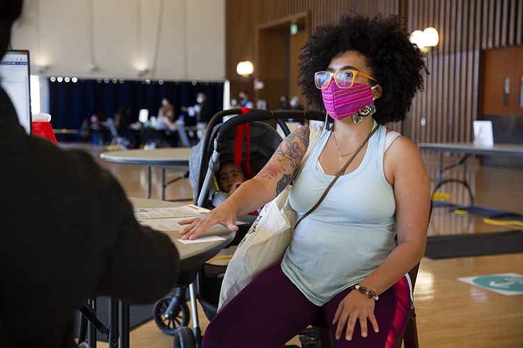 Krista Cortes, a graduate student of color, gets her first COVID-19 vaccine at Pauley Ballroom. She sits in a chair with a bright pink face mask waiting for her shot.