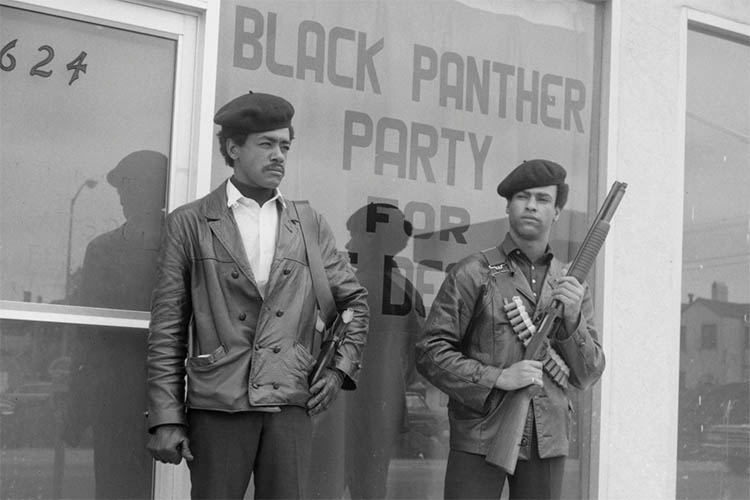 two black men hold guns in front of a window saying 