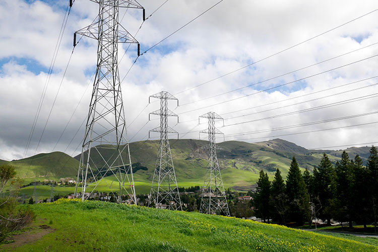 A photo shows large power lives over a hilly landscape