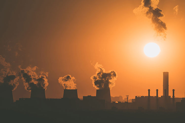 Silhouettes of smokestacks against an orange sunset sky