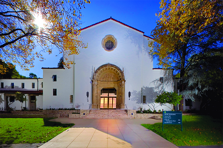 The Littlefield Concert Hall at Mills College is Spanish-style and has lights on insdei of it as night falls.