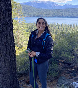 a woman smiles at the camera in front of a lake and mountains 