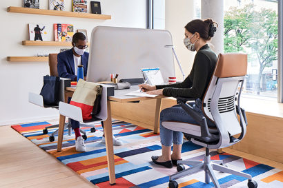 two masked workers sit in a modernistic office
