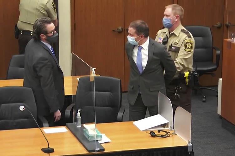 chauvin is held in hand cuffs by an officer while he talks with his attorney in a court room