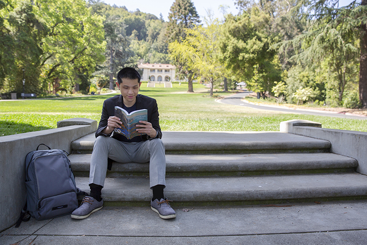 A photo of Berkeley Law doctoral student Alex Mabanta, reading a book on some steps near the law school.