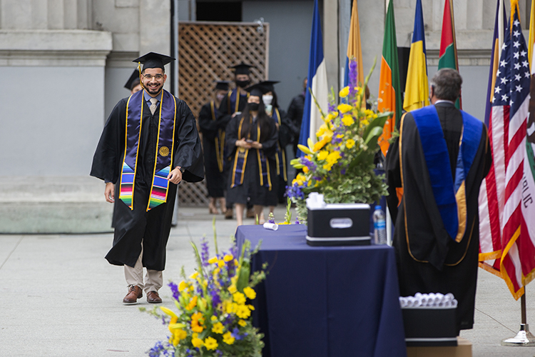 A student crosses the stage at the Greek Theatre wearing regalia and a colorful stole.