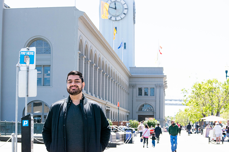 Harris Mojadedi poses and smiles with the Ferry Building in San Francisco behind him.