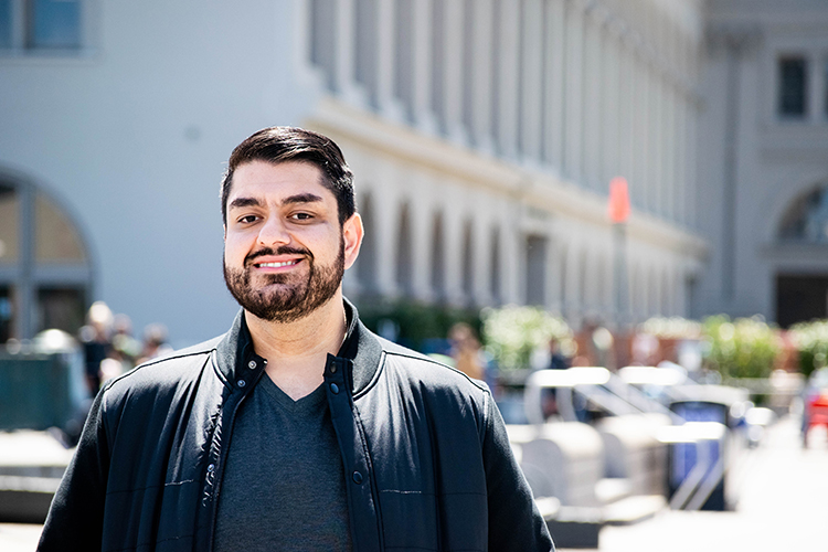 Harris Mojadedi poses and smiles with the Ferry Building in San Francisco behind him.