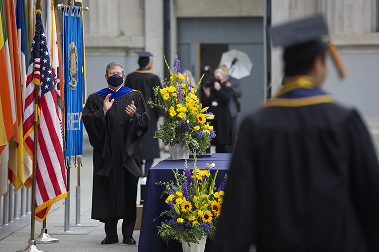 Athletic Director Jim Knowlton, wearing regalia, stands on the dais in the Greek Theatre to greet graduates as they cross the stage.