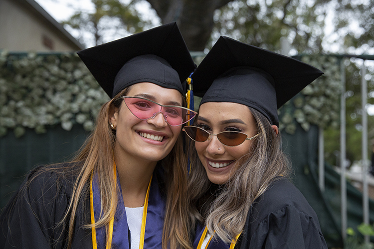 A close-up of two students wearing smiles and fashion sunglasses at the graduation procession.