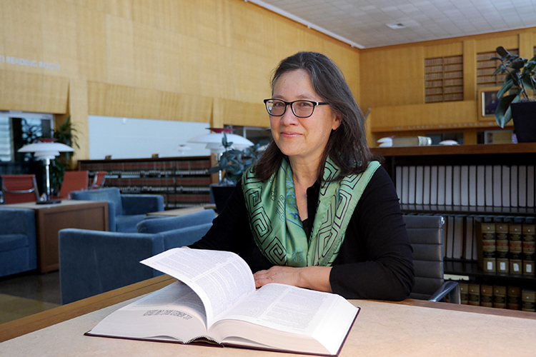 A close-up photo of Leti Volp, professor at Berkeley Law. She is sitting in the law library with eyeglasses and a green scarf around her neck.