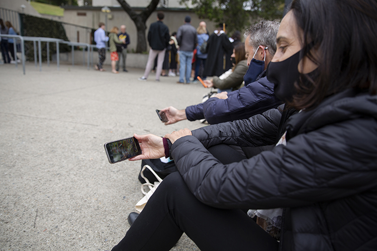 A mother sitting outside the gate of the Greek Theatre watches on her cell phone for the moment her daughter walks across the stage.