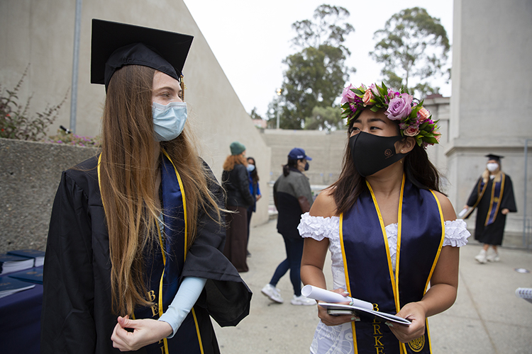 In their regalia and masks, friends Claire Black and Paris Sato visit with each other after the graduation procession.