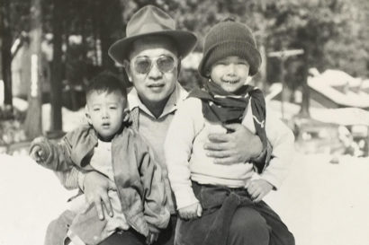 two young boys sitting on their dad's lap outside