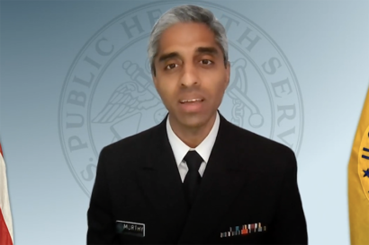 Vivek Murthy speaks in front of two flags