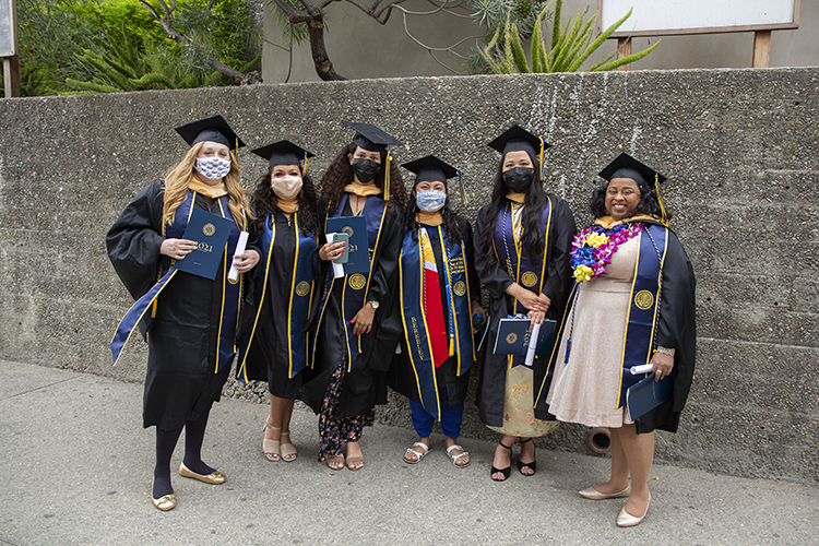 A group of close friends, all Master of Social Work graduates, pose for a photo in their stoles, masks and regalia.