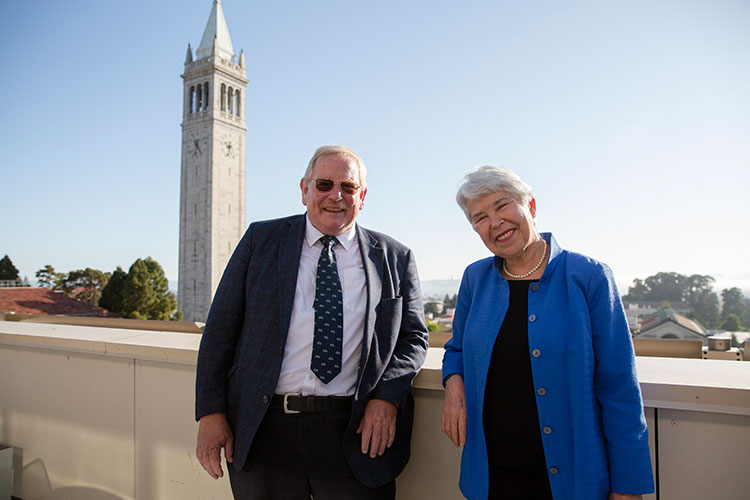 Reinhard Genzel stands beside Chancellor Carol Christ on a campus balcony, with the campanile in the background.