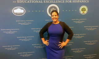 matos standing in front of a blue sign saying "educatiional excellence for hispanics"
