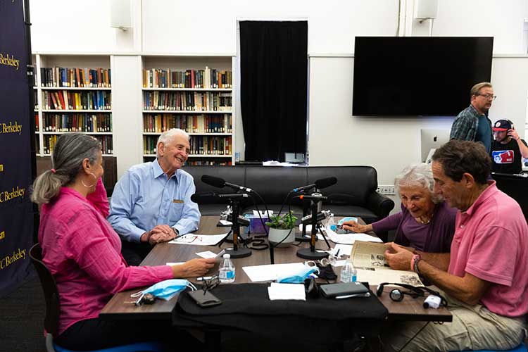 Journalists talking at a podcast desk.