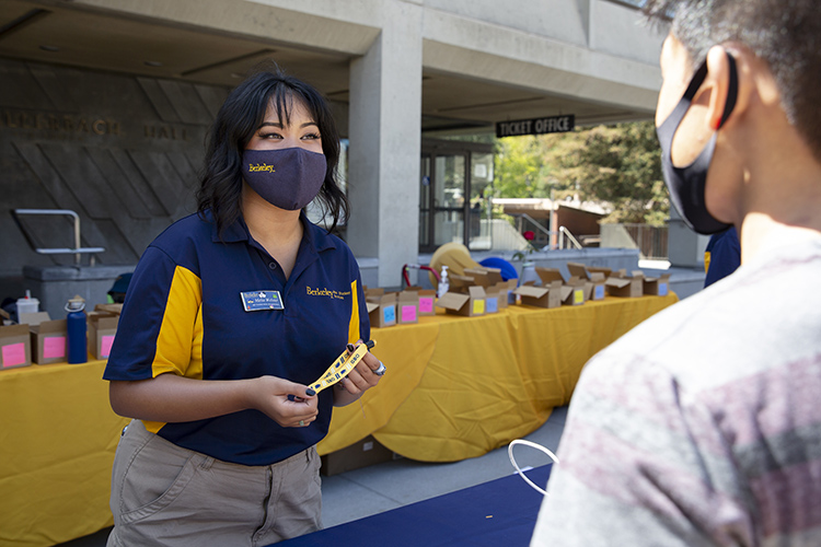 a woman in blue and gold welcomes a new student on lower sproul plaza