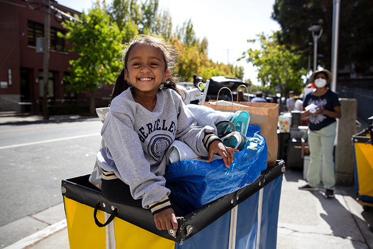 a young person in a berkeley sweatshirt sits in a trolley of items