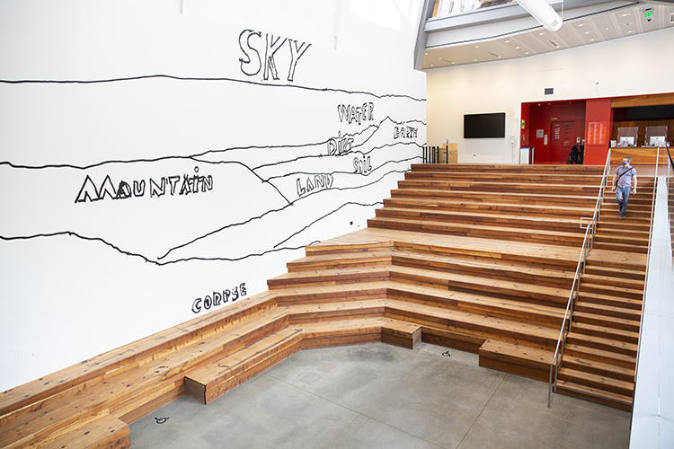 many wooden stairs going down into a gallery space next to an art wall