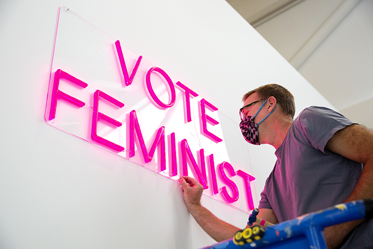 a person works on a bright pink sign that reads 