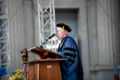 Chancellor Christ stands at the podium on the Greek Theatre stage wearing regalia.