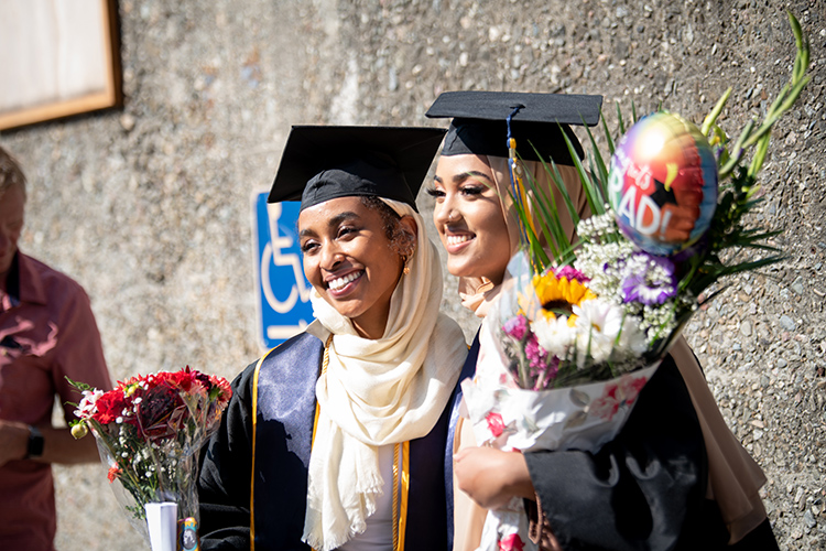 Two women smile for the camera, and one holds a bouquet at the Class of 2020 In-Person Commencement at the Greek Theatre.