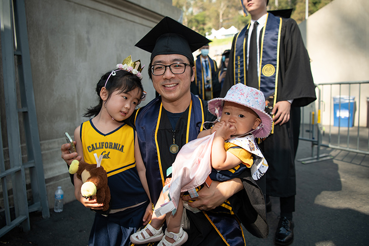 A 2020 grad holds his two young daughters, who are wearing Berkeley colors at the Class of 2020 In-Person Commencement.