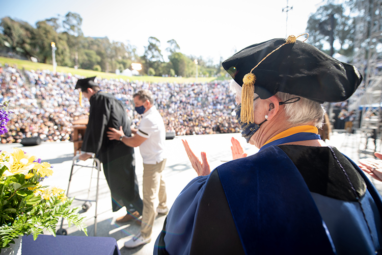 Chancellor Christ, wearing regalia, claps for former Cal Rugby player Rob
