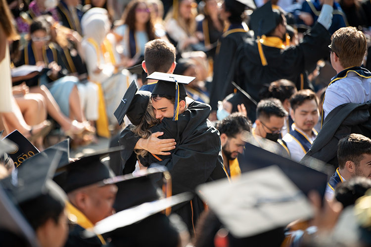 Two 2020 graduates in regalia embrace in the middle of the crowd at the Greek Theatre at the Class of 2020 In-Person Commencement on Sunday, Aug. 29 at the Greek Theatre