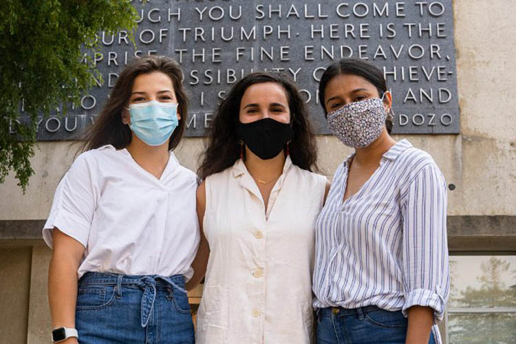 three people in masks stand in front of the Berkeley Law building