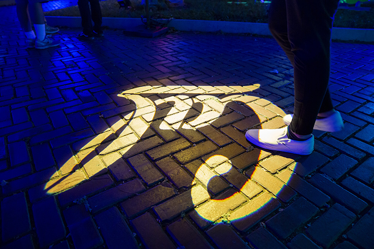 A Cal sign is illuminated in gold on the ground as students walk along Campanile Way during Golden Bear Orientation's Paint the Night event.