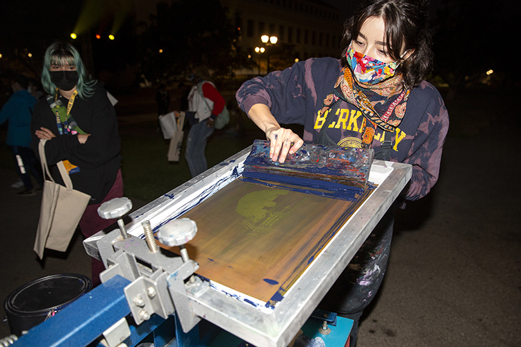 A staff member of the UC Berkeley Art Studio makes screen-printed bags for students during Golden Bear Orientation's Paint the Night event on Friday, Aug. 20. She's wearing a tie-dyed UC Berkeley sweatshirt and is using a screen printer. a