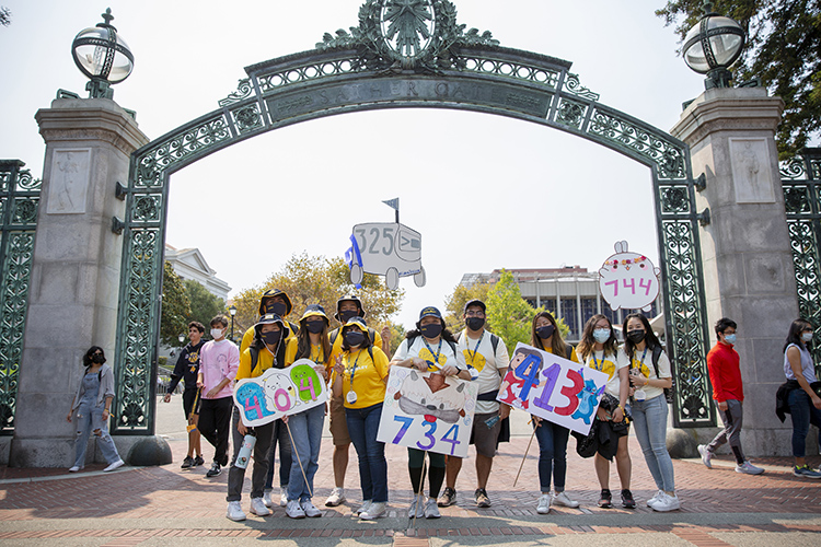 Various GBO leaders stand under Sather Gate with signs that spell out the names of their student orientiation groups.