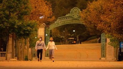 two students, hand in hand, walk across a campus that's empty and bathed in a strange orange light