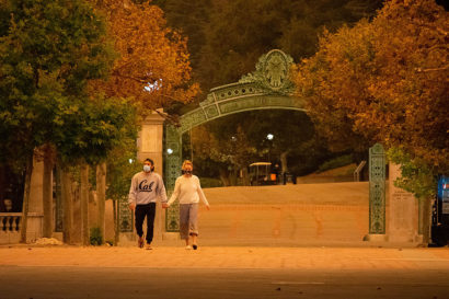 two students, hand in hand, walk across a campus that's empty and bathed in a strange orange light