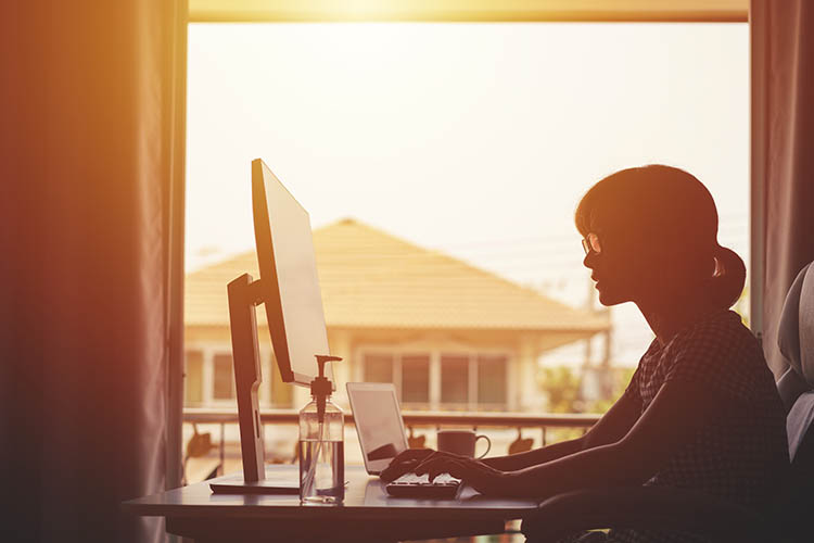 woman working from home in the sun while sitting at a computer