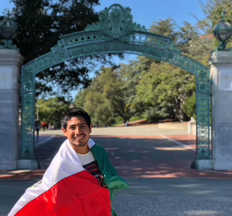 Artemio Orta with a Mexican flag wrapped over his shoulders in front of UC Berkeley's Sather Gate.